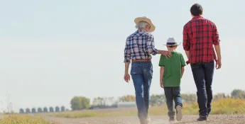 Three people in casual clothing walk down a dirt path in a rural area, where fields and trees frame the scenic backdrop. They chat amicably about animal ag practices, their laughter blending with the sounds of nature around them.