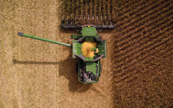 An aerial view captures a green combine harvester efficiently collecting corn in the field, showcasing farm business management at its finest, with half the crop harvested and half unharvested.