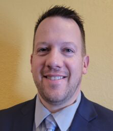 A man in a suit and tie smiles at the camera against a yellow background, radiating confidence as he promotes innovative farm program services.