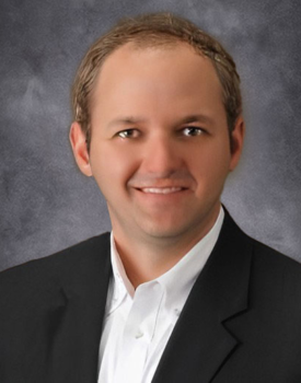 A smiling Thomas in a suit and white shirt stands confidently against a gray background, exuding the expertise of farm business management.
