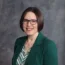 Baalman Lisa with a green blazer and patterned shirt, standing against a grey backdrop.