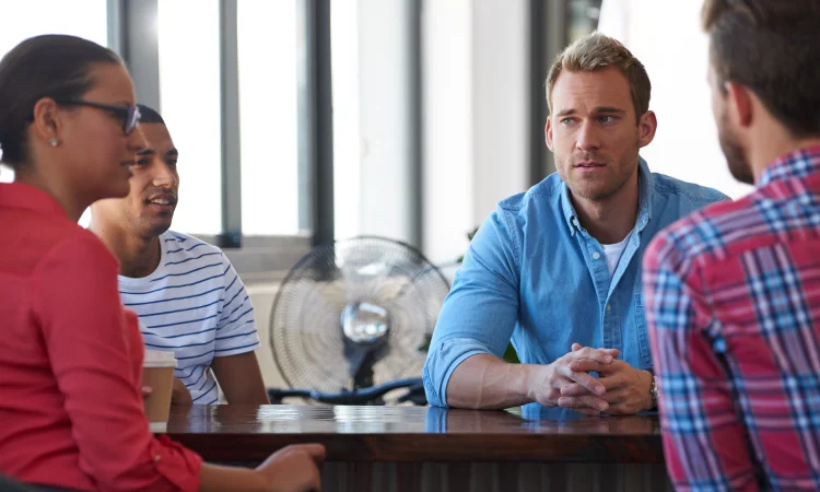 Four people are sitting around a table in a brightly lit room, engaged in a lively discussion, embodying the dynamic energy of peer groups.