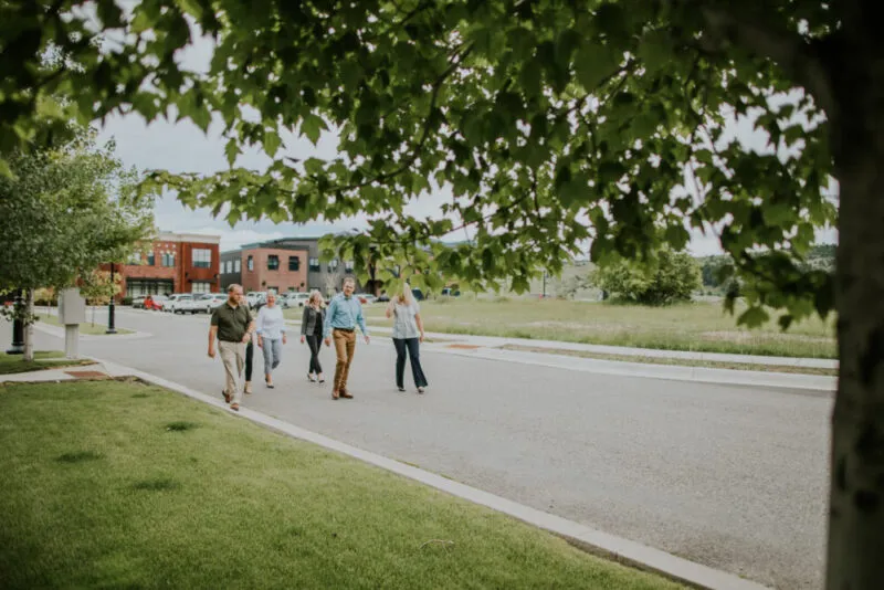 A group of people walking on a sidewalk in a suburban area, with trees and modern houses in the background.