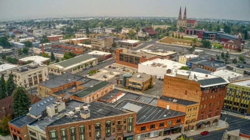 Aerial view of an urban area featuring a mix of historical and modern buildings, roads, and a prominent cathedral in the distance under a hazy sky.
