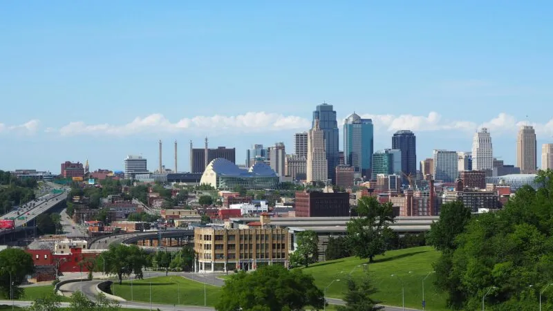 Skyline of Kansas City with tall buildings, green spaces, and highways under a clear blue sky.