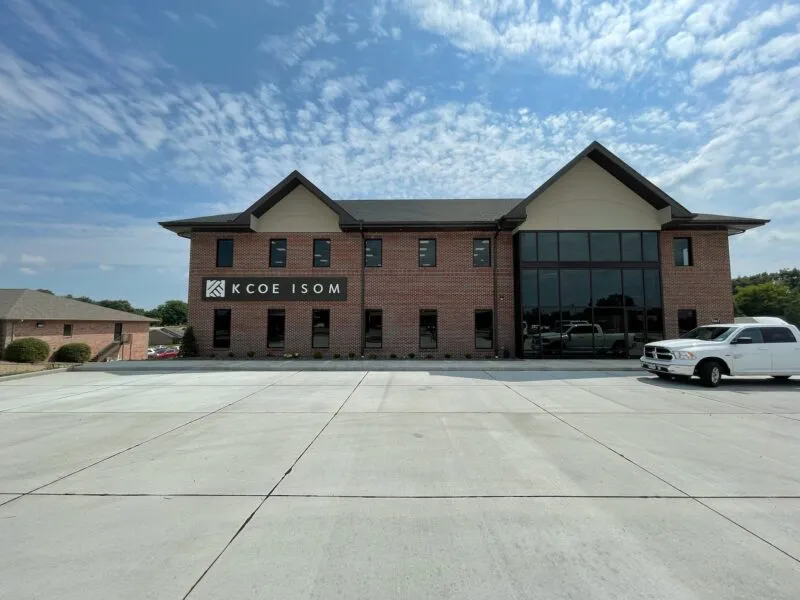 A brick office building with a sign saying "KCoe Isom" on the facade. A white pickup truck is parked in front, under a partly cloudy sky.