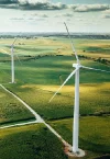 Two wind turbines stand majestically in a vast green field under a cloudy sky, with a road running alongside—an impressive sight for any land advisory team assessing sustainable development opportunities.