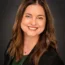 Michelle Ellis with long brown hair smiling, wearing a dark blazer and green top against a dark background, exuding confidence and professionalism, reminiscent of someone ready to excel in transactional advisory.