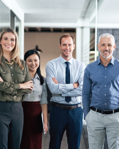 Four people are standing in an office hallway, smiling with the confidence of successful financial institutions behind them. Two women and two men, dressed in business casual attire, exude professionalism and camaraderie.
