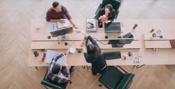 An above view of a group of four people who are seated around a conference table.