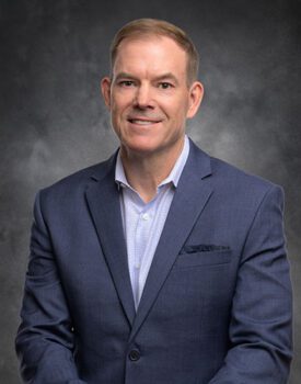 A person in a blue suit and white shirt, embodying the expertise of transactional advisory, smiles confidently at the camera against a dark backdrop.