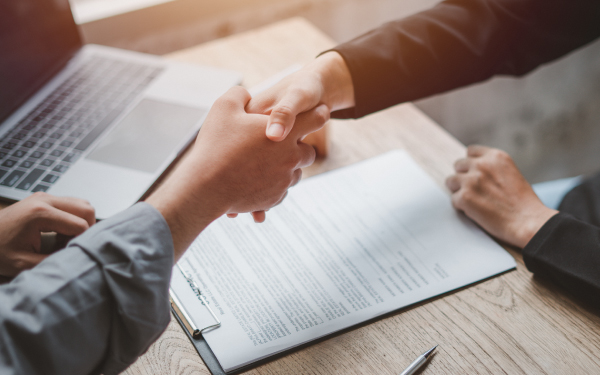 Two people shaking hands over a signed contract