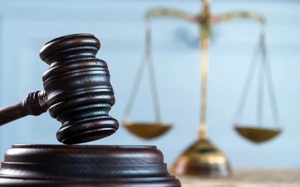 A wooden gavel rests prominently in the foreground, with a blurred set of balance scales and forensic accounting reports scattered about in the background, symbolizing justice.