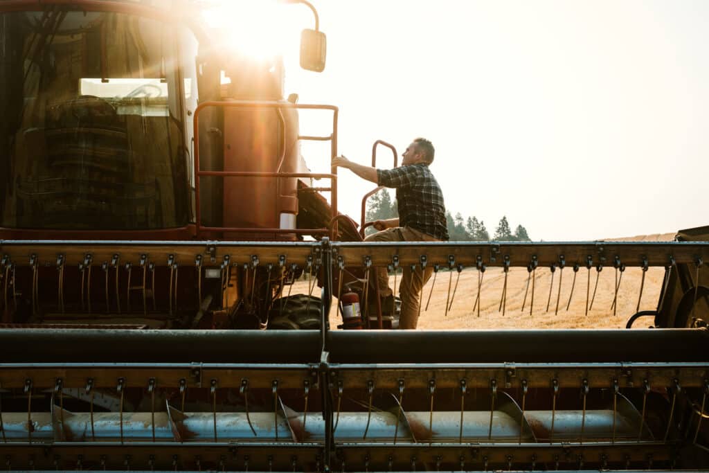 A farmer climbs up the ladder into his large combine grain harvester, ready to start a long day of work. The morning sun rises just behind him.  Shot in Worley, Idaho, USA.