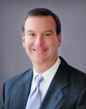 Alan Grafton, a man in a suit and tie, smiles warmly against a plain background.
