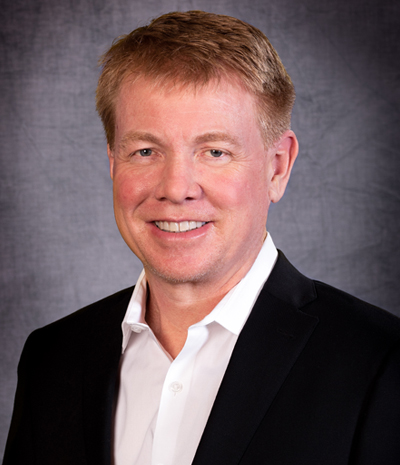 Chris Haverkamp, with short light brown hair, wearing a black suit and white shirt, smiles warmly against a gray background.