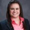 Kristen Glasgow beams with confidence in a black blazer and pink shirt against a gray background.