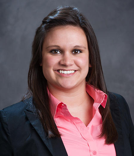 Kristen Glasgow beams with confidence in a black blazer and pink shirt against a gray background.