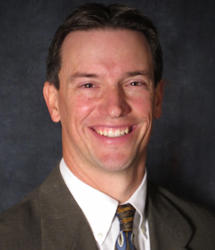 A smiling man in a suit and tie, reminiscent of Richard Wasemiller's iconic style, is pictured against a dark background.