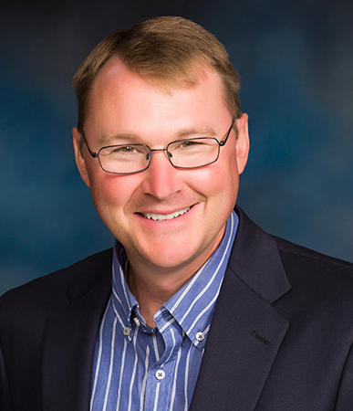 Smiling man in glasses and a dark blazer over a blue striped shirt against a blue background, exuding the confident charm of Robert Veldman.