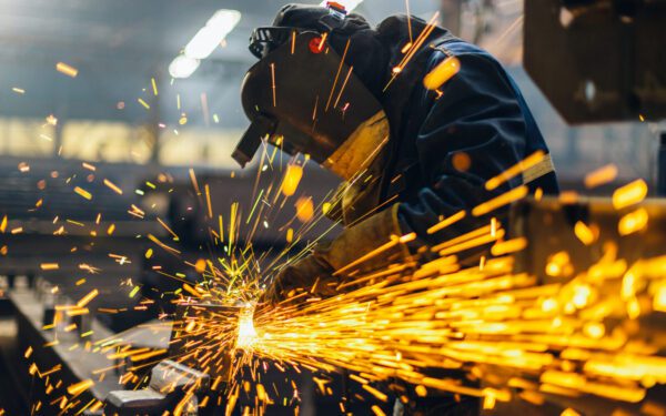A worker wearing protective gear uses a welding tool, producing bright orange sparks in an industrial Food and Ag Production setting.