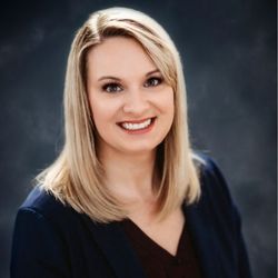 Megan Johnson, a smiling woman with straight blonde hair, wears a dark blazer against a gray backdrop.