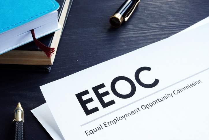 An EEOC document lies on the desk alongside EEO-1 data, accompanied by a pen and notebooks, reflecting Equal Employment Opportunity Commission material.