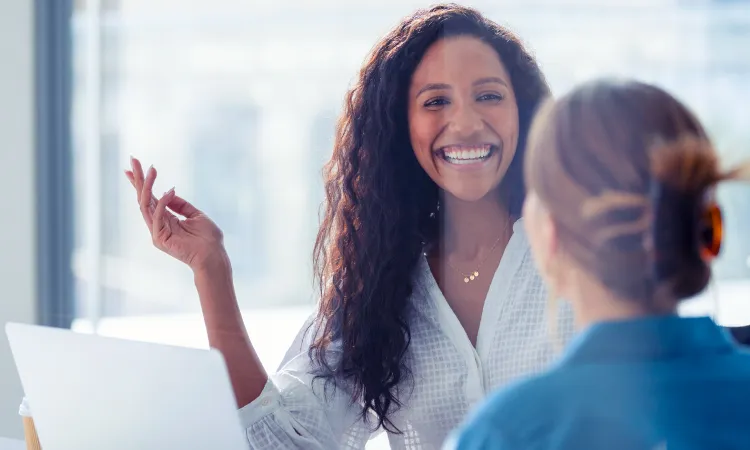two professionally dressed women looking at each other and smiling