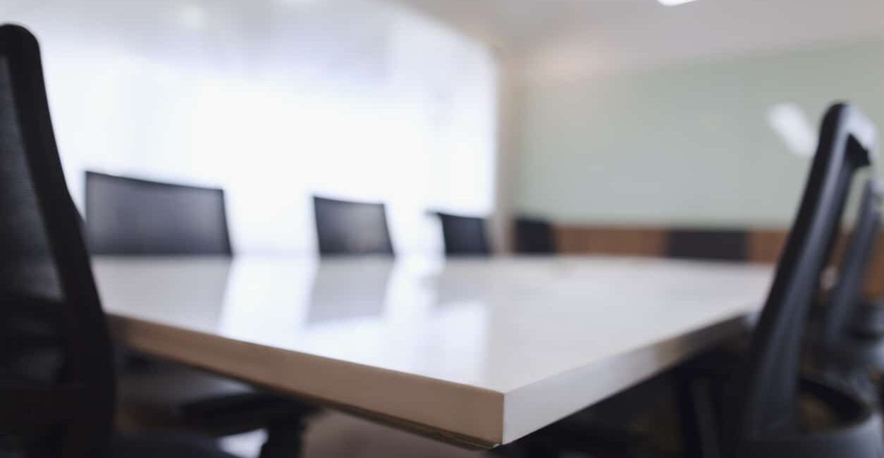 A modern conference room designed for a board of directors, featuring a large rectangular table and several sleek black office chairs around it. The space is bathed in natural light streaming through a generous window.
