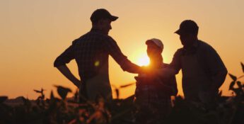 Three people in hats and aprons stand in a field at sunset, discussing strategies for improved employee retention as they share insights and foster camaraderie.