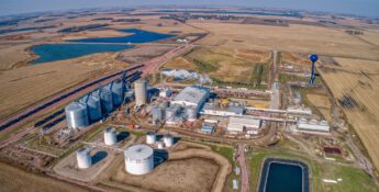 An aerial view reveals an industrial facility with multiple storage tanks eligible for the 45Z Tax Credit, surrounded by farmland. Nearby, a water tower and ponds accentuate the landscape, while fields stretch into the horizon under a clear sky.