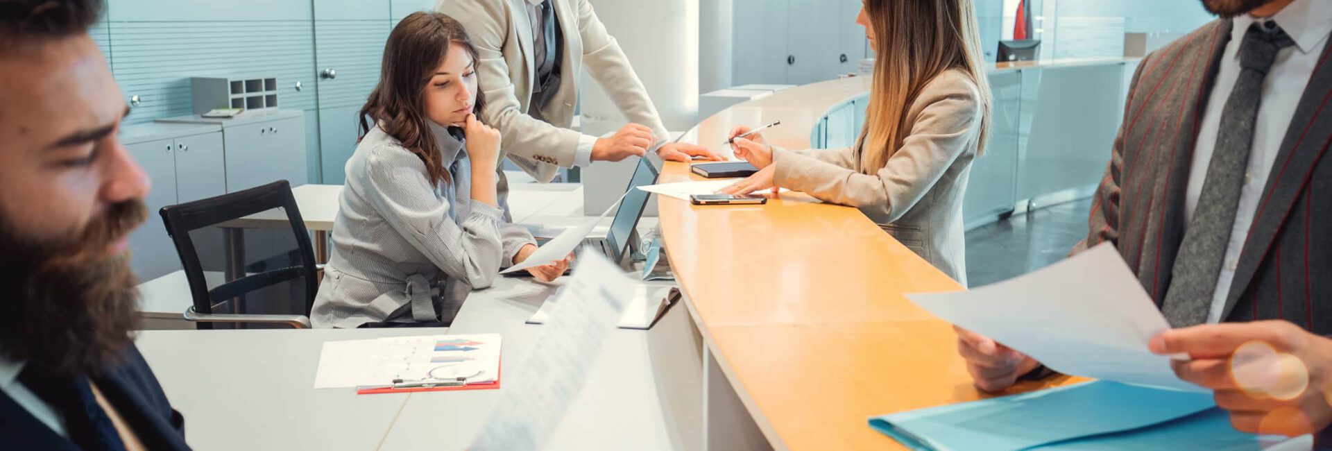 A group of people in business attire are gathered around a table with laptops and documents in an office setting, appearing engaged in a discussion on internal controls.