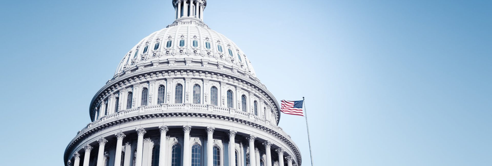 U.S. Capitol building dome with American flag against a clear blue sky.