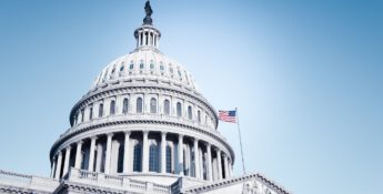 U.S. Capitol building dome with American flag against a clear blue sky.