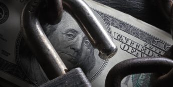 A hundred-dollar bill is partially visible beneath a chain and padlock, the lock open, symbolizing how to increase business wealth by overcoming financial restriction or enhancing security measures.
