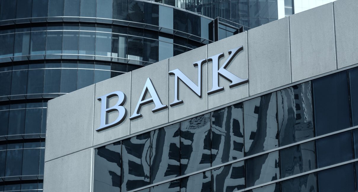 Exterior of a modern bank building with reflective glass windows and a large "BANK" sign on the facade, showcasing its commitment to FDICIA compliance.