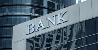 Exterior of a modern bank building with reflective glass windows and a large "BANK" sign on the facade, showcasing its commitment to FDICIA compliance.