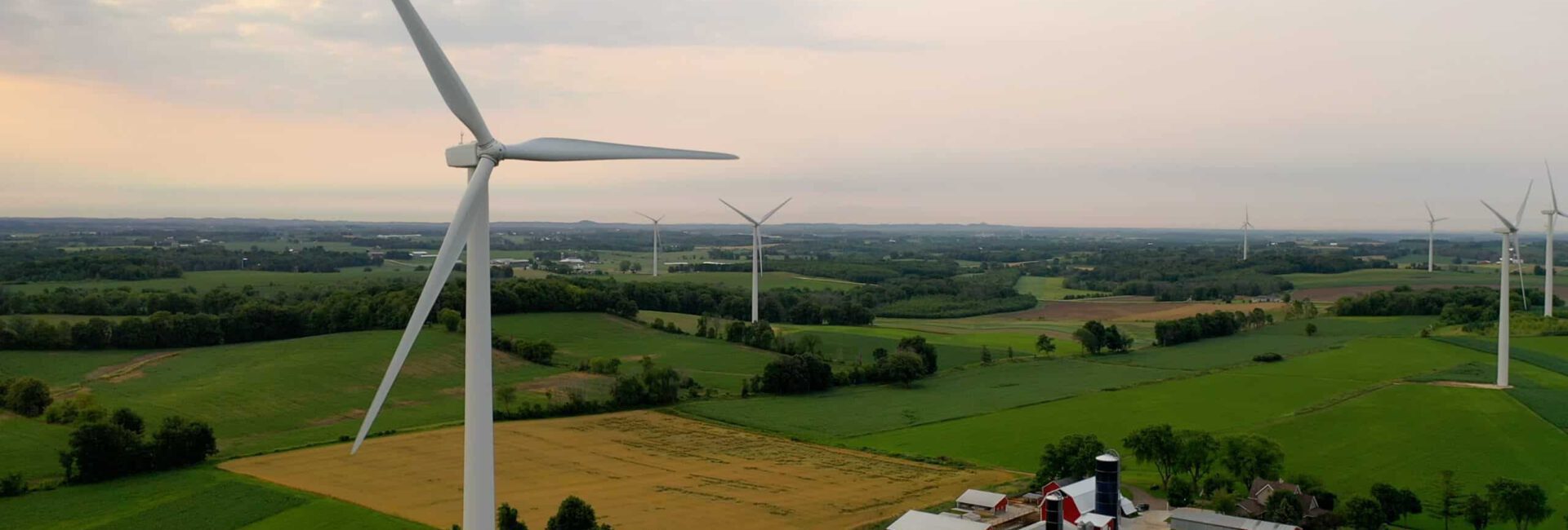 Wind turbines stand tall across a rural landscape of fields and farms, embodying a commitment to land stewardship under a cloudy sky.