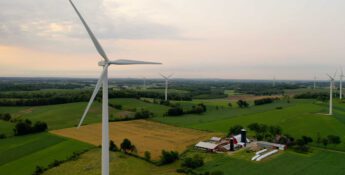 Wind turbines stand tall across a rural landscape of fields and farms, embodying a commitment to land stewardship under a cloudy sky.