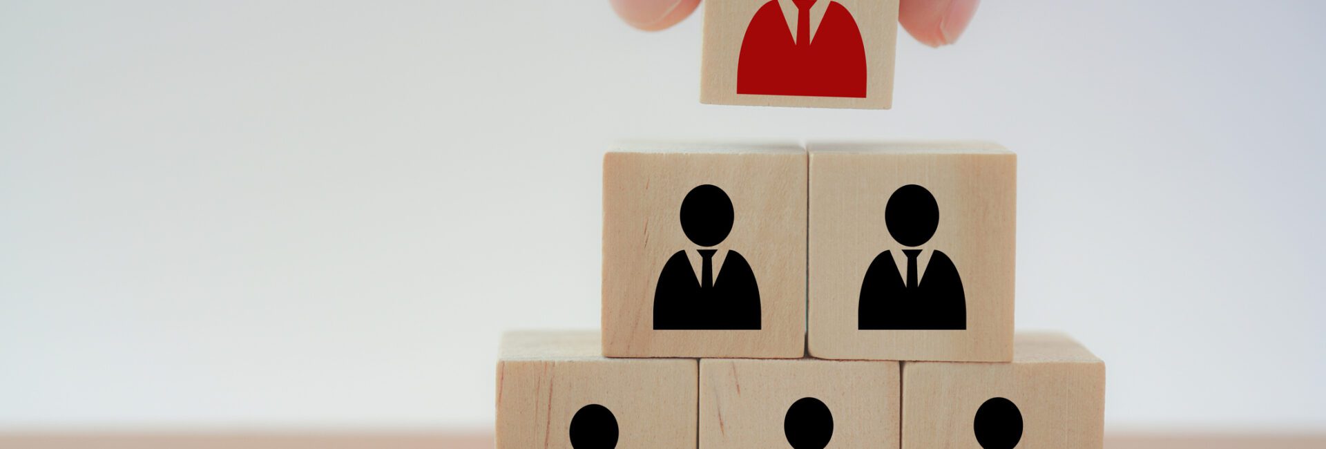A hand places a red figure block atop a pyramid of black figure blocks, representing leadership or hierarchy.