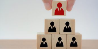 A hand places a red figure block atop a pyramid of black figure blocks, representing leadership or hierarchy.