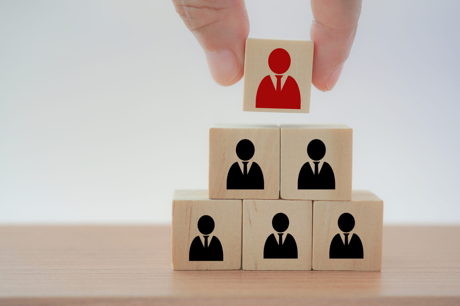 A hand places a red figure block atop a pyramid of black figure blocks, representing leadership or hierarchy.