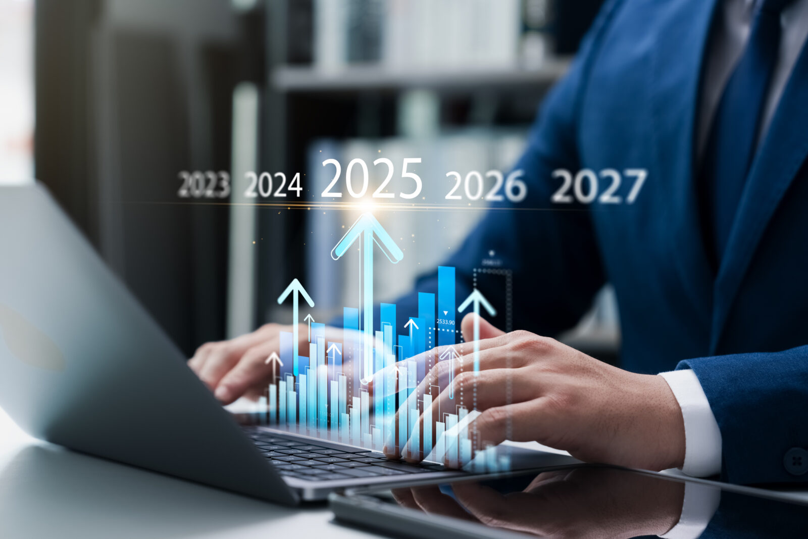 Person using a laptop with a graph overlay, indicating rising trends from 2023 to 2027.