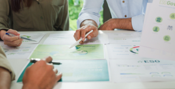 Three people reviewing ESG-related documents and graphs at a table, with one person pointing to a green chart with a pen.
