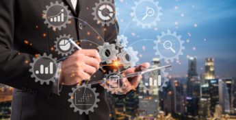 Businessperson using a digital tablet overlaid with holographic gears and charts, symbolizing technology and data analytics, with a cityscape in the background.