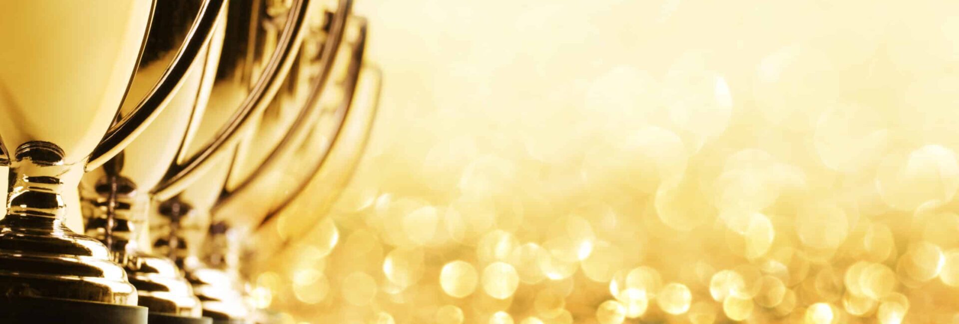 Row of gold trophies with blurred golden bokeh background.