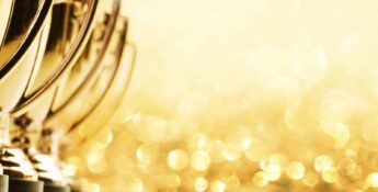 Row of gold trophies with blurred golden bokeh background.