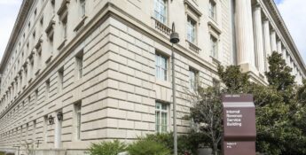 A large, beige stone building with multiple windows, identified by a nearby brown sign as the Internal Revenue Service Building.