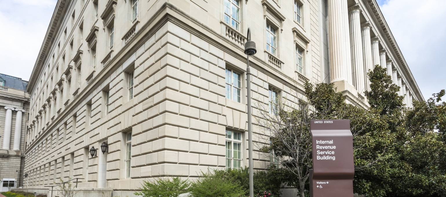 A large, beige stone building with multiple windows, identified by a nearby brown sign as the Internal Revenue Service Building.