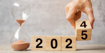 A hand flips a wooden block from 2024 to 2025, symbolizing the transition to a new year. An hourglass filled with sand sits beside it, reminding us of the importance of time management as part of essential HR year-end tips.